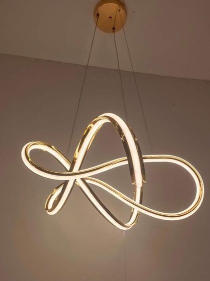 An abstract ribbon-style chandelier in a gold finish. The flowing, continuous loop of light creates a sense of motion and artistry.