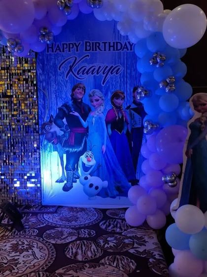 A close-up of a Frozen backdrop with the main characters, framed by a blue and purple balloon garland.