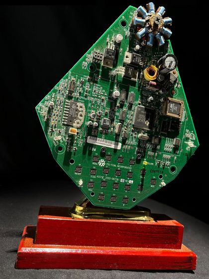This award features a green circuit board mounted on a red wooden base, crowned with a cluster of capacitors. Each piece is a one-of-a-kind masterpiece of design and innovation.