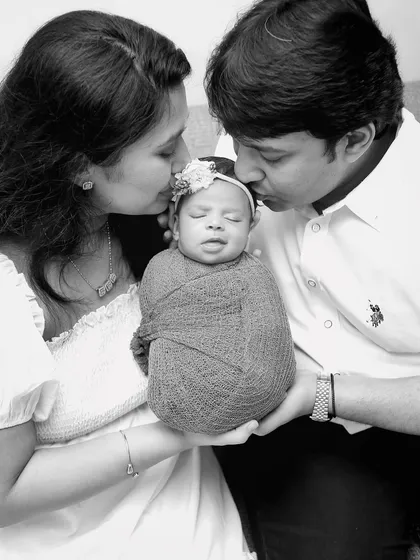 A timeless black and white portrait of parents kissing their newborn's head. This classic pose emphasizes the love and protection surrounding the newest family member.