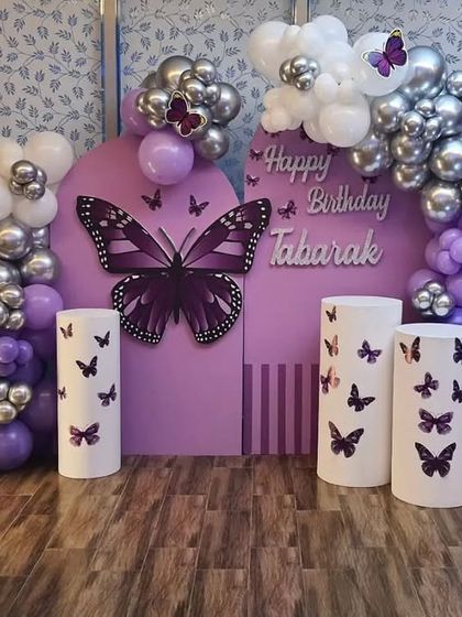A chic and modern take on the butterfly theme with a purple and chrome silver balloon arrangement. The custom backdrop and plinths are decorated with butterfly graphics, paired with a large marquee number '1'.