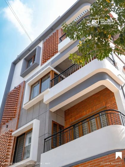 An upward-looking shot of the Akshaynagar facade, emphasizing the curved balcony lines and the textural contrast of the brickwork.