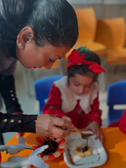 An instructor helps a young girl add chocolate to her cookie.