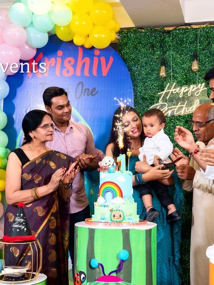 A happy family celebrating their son's first birthday with a Cocomelon themed cake and decor.