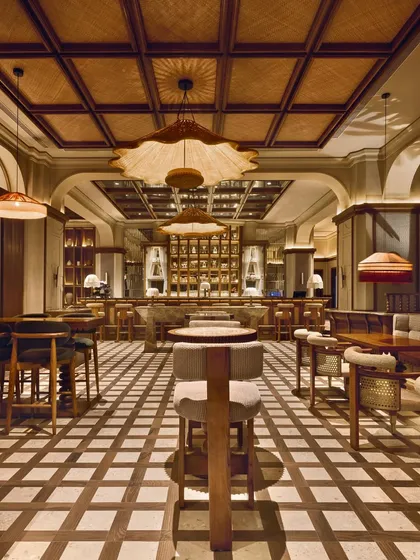 The main dining area, where a checkerboard floor and a ceiling of woven rattan create a rich, textured environment. The space is designed to feel both communal and intimate.