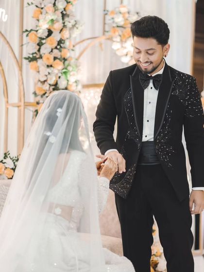 A sweet moment during the ring ceremony. The groom holds the bride's hand, his expression full of love and admiration as she looks down with a smile.