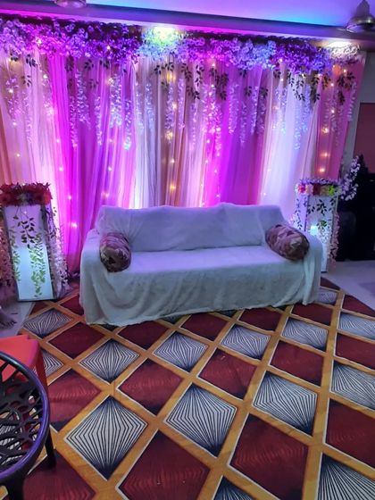 A cozy decor setup for a house party or small gathering, with a purple-lit backdrop of hanging flowers and a comfortable sofa.