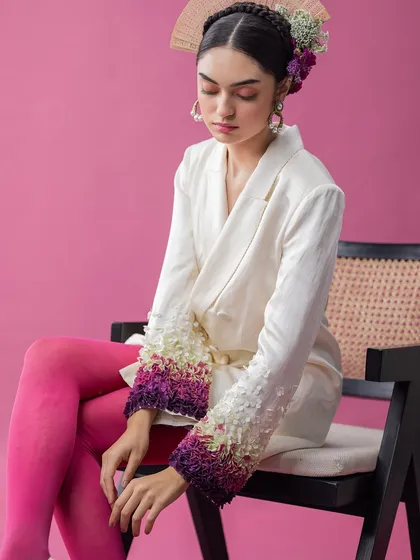 A full look from an avant-garde series, this image combines a sharply tailored blazer with bold, colorful tights. The contrast between the structured jacket and the vibrant legwear, along with the floral headpiece, creates a visually arresting, high-fashion statement.