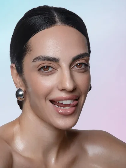 A joyful, candid moment that still showcases the professional makeup application. The glossy skin and lips catch the light beautifully, creating a vibrant and energetic feel.