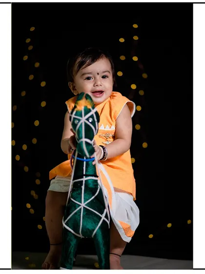A front-facing portrait from a studio session with a prop horse. The dark background makes the child and the vibrant colors of his outfit stand out.