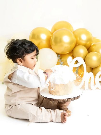 A classic and elegant first birthday setup with gold and cream balloons. This little one is gently exploring his giant cupcake before the real smashing fun begins.