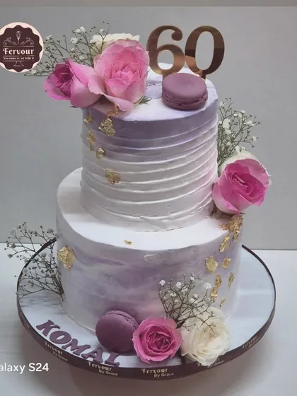An elegant two-tier cake to celebrate a 60th birthday. This chocolate truffle cake has a lavender ombre design and is decorated with fresh roses, baby's breath, and macarons.