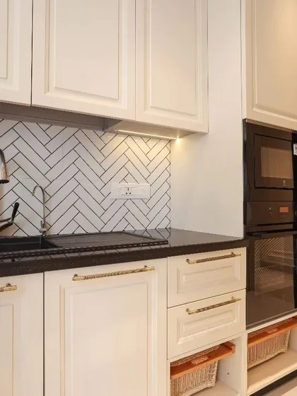 This shot highlights the functional aspects of a classic kitchen design, including an integrated oven and microwave tower, a deep sink, and open wicker basket drawers for vegetable storage.