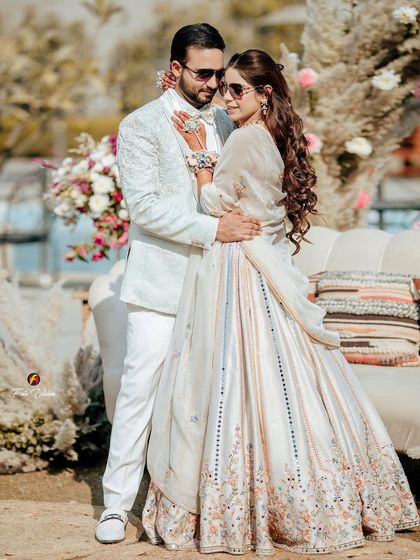 A classic romantic pose of the couple at their Mehendi, embracing in front of a beautiful floral and pampas grass backdrop.