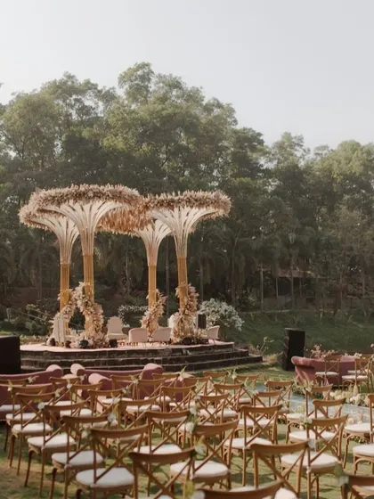 An exquisite mandap with unique, tree-like structures covered in pampas grass and florals, creating a whimsical yet sophisticated look for an outdoor wedding.