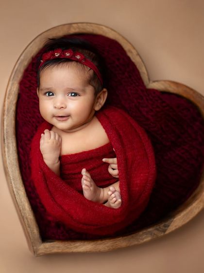 A beautiful baby girl wrapped in red, smiling softly in her sleep. The neutral background makes the rich color and her expression pop.