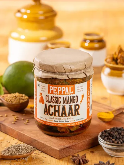 A vibrant shot of Peppal's Classic Mango Achaar, surrounded by whole spices and a raw mango. This styling communicates the product's fresh, authentic ingredients.