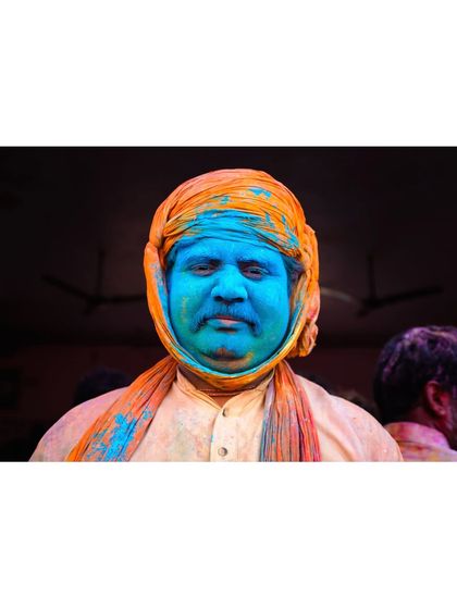 A man's face, completely covered in blue powder, stares calmly at the camera. The contrast between the vibrant color and his serene expression is what makes this portrait compelling.