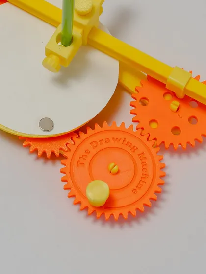 A close-up on the gears of the drawing machine. The center gear is embossed with "The Drawing Machine" text.