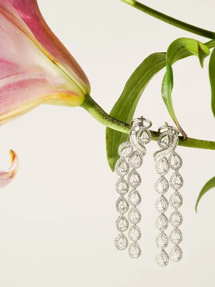 A pair of magnificent cascading diamond earrings hangs delicately from a lily stem. This creative composition emphasizes the jewellery's elegance and connects it with natural beauty.