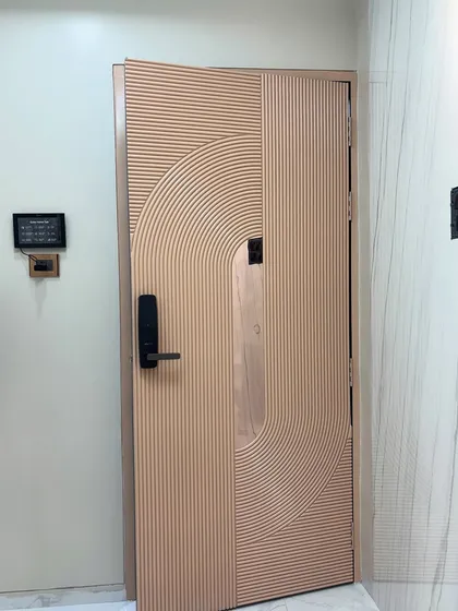 A unique main door with a textured, fluted design in a soft rose gold finish. The wave-like pattern creates a dynamic and artistic first impression.
