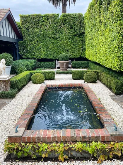 A formal brick-edged pond serves as a beautiful focal point in this courtyard. The design is highly symmetrical, with gravel paths, clipped hedges, and a statue creating a sense of classical order.