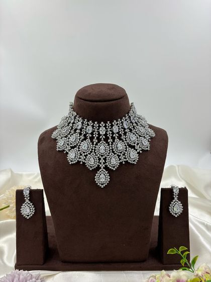 A heavy, silver-plated AD necklace set with a peacock-inspired feather design. This statement piece is available in blue, green, pink, and all-white.