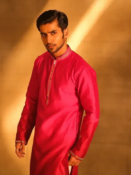A portrait of a groom in a vibrant pink kurta. The makeup is subtle yet effective, evening out his skin tone and ensuring he looks sharp and photogenic under the studio lights.