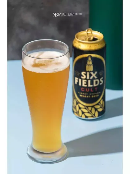 A chilled glass of Six Fields Cult wheat beer next to its can. The clean, bright lighting and simple background make this a perfect commercial shot for beverage advertising.