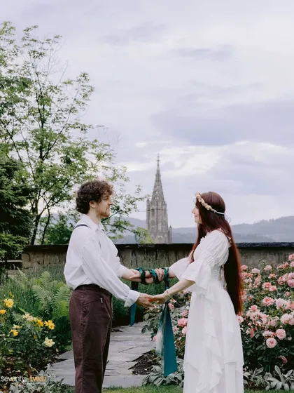 In a beautiful garden in Bern, they perform a hand-fasting ceremony. This wide shot captures the ancient Celtic ritual against a timeless Swiss backdrop.