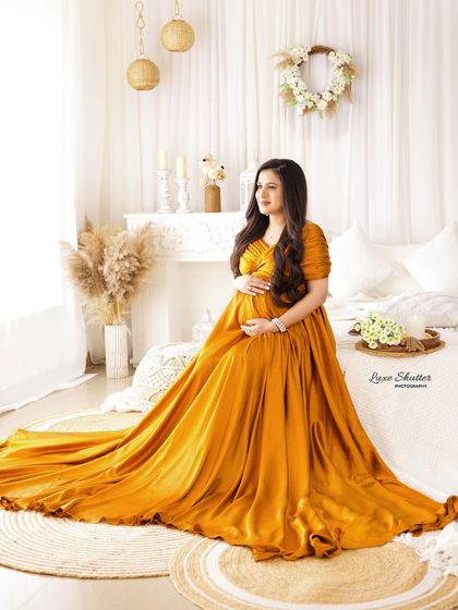 A full view of this stunning mustard-colored satin gown, its train spread beautifully across a boho-style studio set.