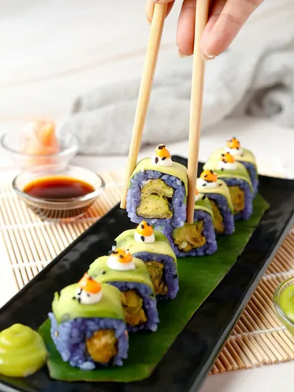 A colourful and creative sushi roll with purple rice being picked up by chopsticks.