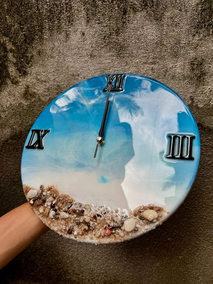 A slightly different angle of the ocean wall clock, showing how the light reflects off the glossy surface. The details of the shells and sand at the bottom bring a piece of the beach into your home.