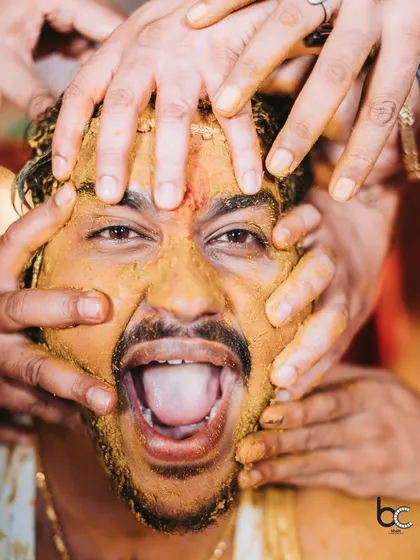 The pure, unadulterated chaos and joy of a Haldi ceremony. This close-up captures the groom's priceless expression as his friends and family lovingly smother him in turmeric paste.