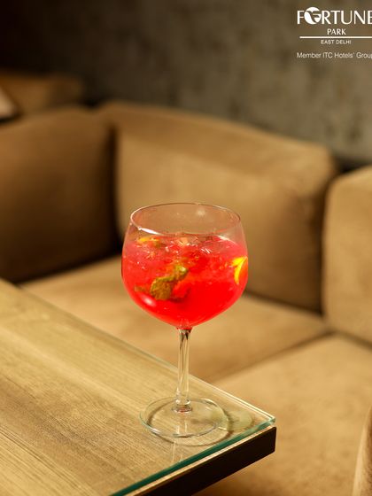 A close-up of a bright red cocktail on a glass table, reflecting the warm, ambient light of the lounge.