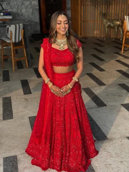A full-length shot showcasing the bride's complete monochrome red look. The makeup is balanced to be impactful yet elegant, ensuring it complements the heavily embroidered lehenga without overpowering it.