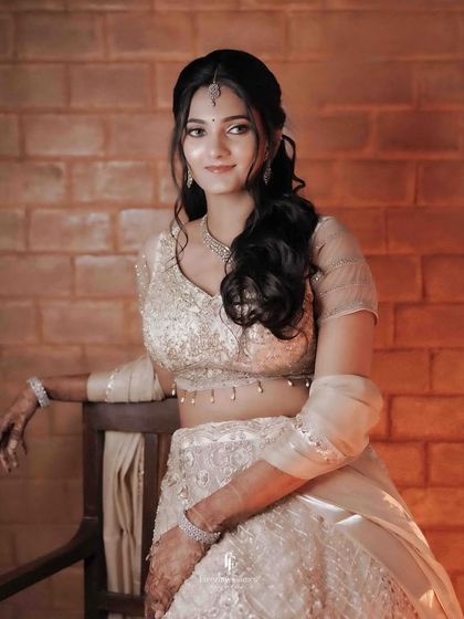 A beautiful portrait of the bride in a light-colored lehenga against a brick wall, her expression serene.