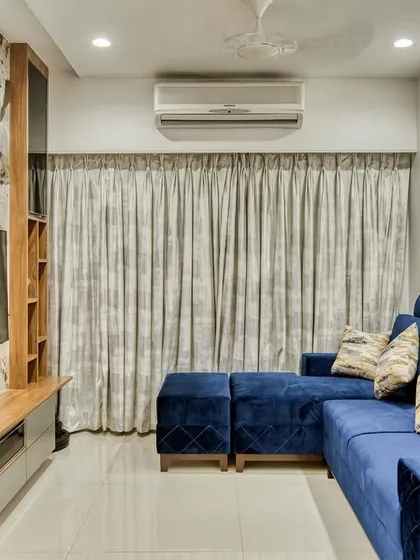 The living room setup with a comfortable L-shaped blue sofa and elegant curtains. We create spaces that are perfect for relaxing and spending time with family.