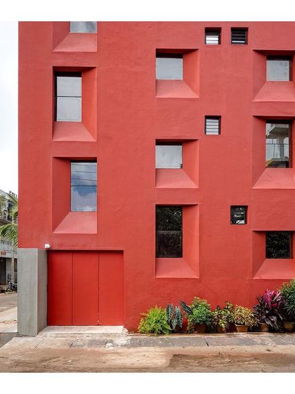 The entrance to the "Stacked Student Housing" is subtly integrated into the powerful red facade, with a small garden softening the transition from the street.