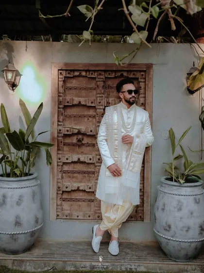 The groom, styled in a classic white sherwani, against a backdrop of traditional architecture. I work to create portraits that are not just photos, but reflections of personality and heritage.