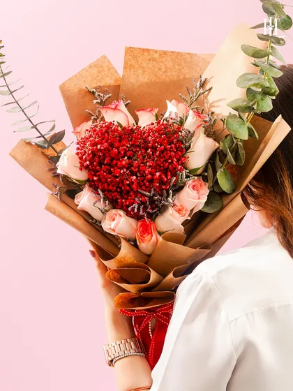 A bouquet where hundreds of mini hearts bloom. This arrangement features a heart made of tiny red flowers, surrounded by soft pink roses, all wrapped in rustic kraft paper for a romantic and natural look.