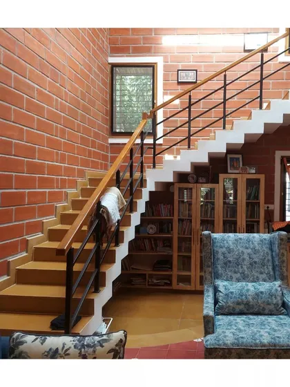 A living space featuring a folded plate staircase, hollow clay block walls, and Athangudi tile flooring.