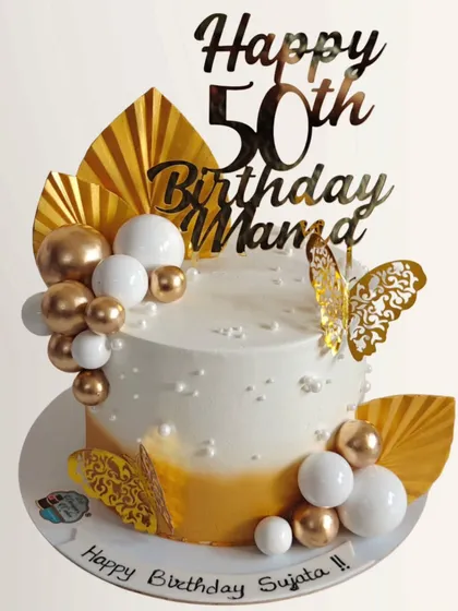 An elegant white and gold cake for a 50th birthday. The design is decorated with golden fans, chocolate spheres, and a butterfly for a sophisticated look.