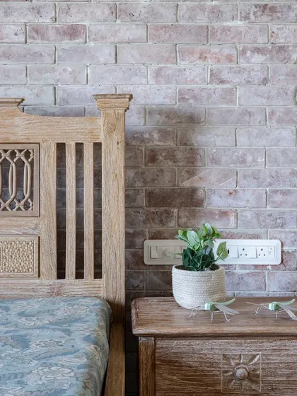 A close-up of the bedroom, showing the texture of the whitewashed brick wall against the intricately carved wooden bed frame. Small details, like the dragonfly ornaments, add a touch of whimsy.