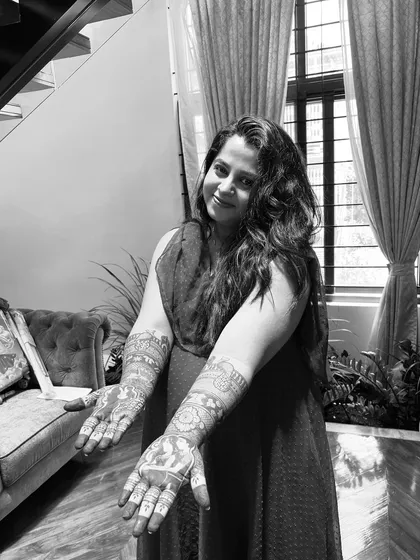 A black and white portrait of a happy client displaying her intricate baby shower henna. The detailed artwork on both hands tells a story of love and anticipation.