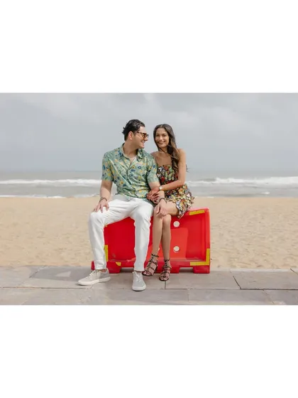 A candid portrait of Saumya and Sid on a bright red beach barricade. The vibrant color and their relaxed pose create a fun, modern, and slightly quirky wedding portrait.