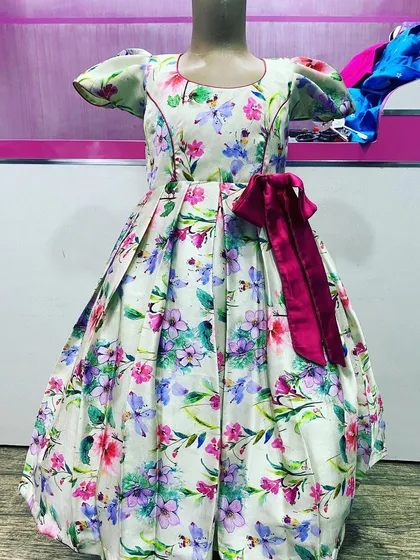 This is a custom-stitched floral frock with box pleats and puff sleeves. The large magenta bow at the waist adds a nice party look, and the fabric is comfortable for kids.