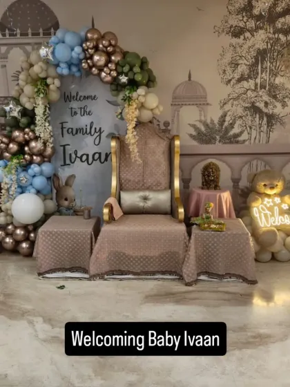 A grand and royal-themed 'Welcome Home' party for baby Ivaan. This setup features a beautiful throne, a custom backdrop, and an elaborate balloon arch in a sophisticated color palette of blue, green, and bronze.