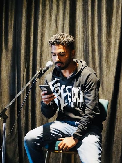 A poet or spoken word artist shares his work from his phone. Our stage welcomes all forms of creative expression, providing a space for every voice to be heard.
