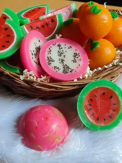 My fruit-themed soaps look almost good enough to eat. This basket shows a variety of my creations, including watermelon, dragon fruit, and orange soaps, all handmade with nourishing ingredients and vibrant, fun designs.